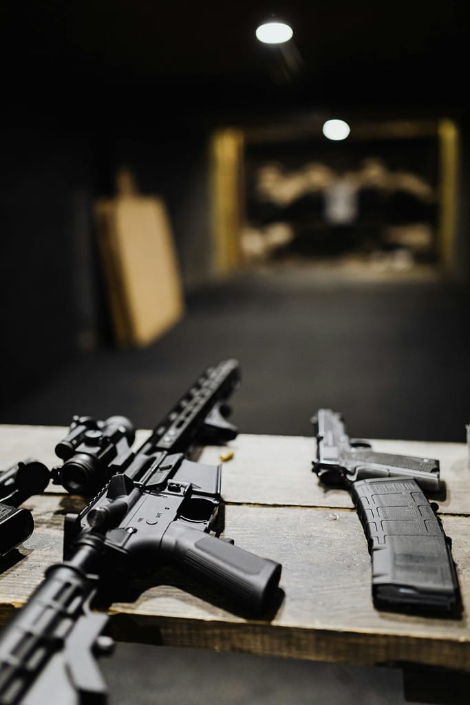 pexels-photo-5202418-5202418 Assault rifles and handguns on a table at an indoor shooting range.